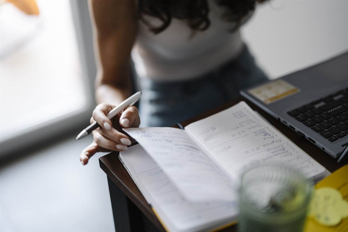 Close-up of a hand taking notes in a notebook next to a laptop