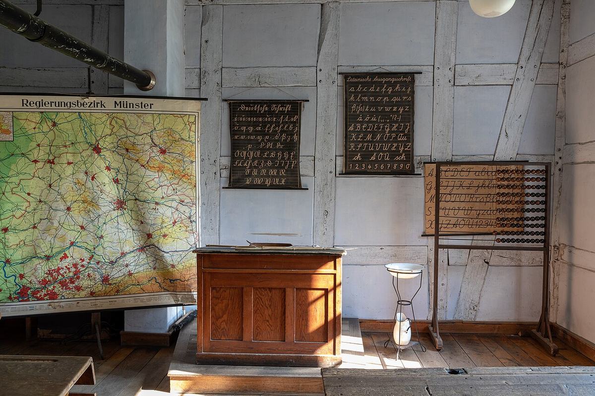 Salle de classe rurale ancienne conservée dans un musée : pupitre de maître en bois, carte murale scolaire, tableaux d’écriture au mur et boulier