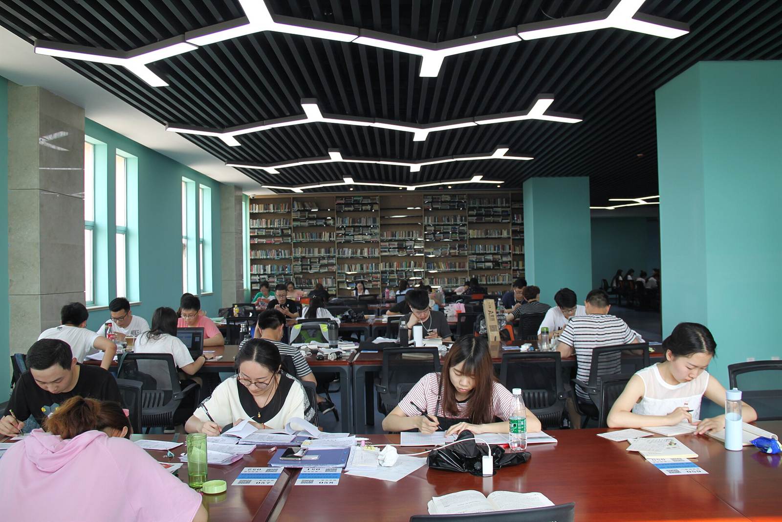 Large university library reading room where dozens of students work on their notes, bookshelves in the background