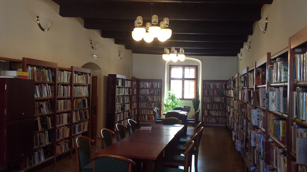 Salle de lecture d’une bibliothèque municipale, longue table de bois et chaises vides, rayonnages pleins sur les deux murs